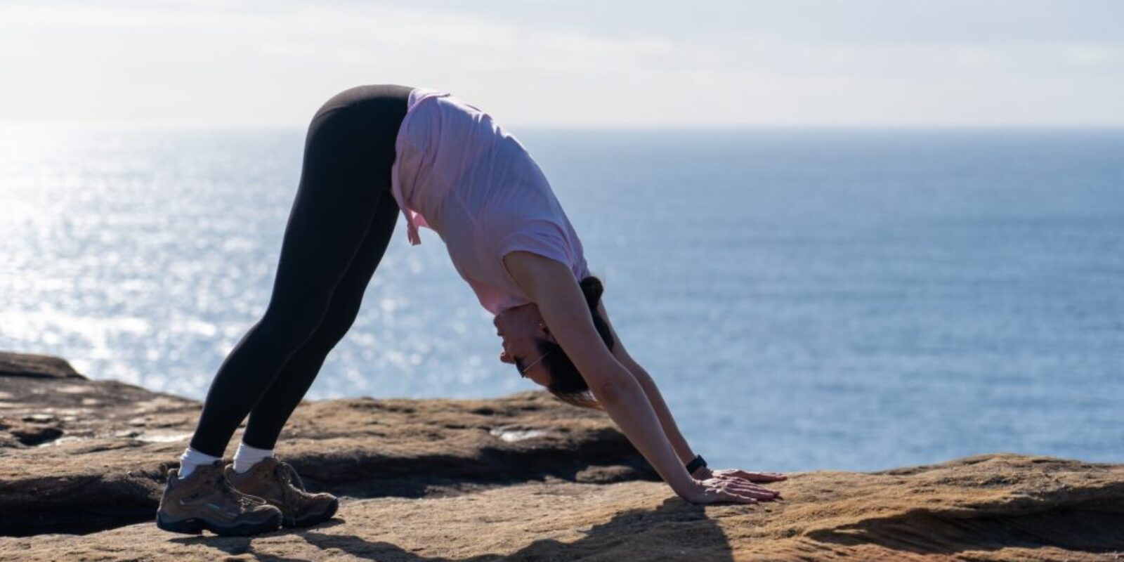 young-woman-lady-practicing-yoga-on-a-cliff-overlooking-the-ocean-at-sunrise-downward-dog-pose